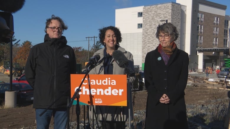 Woman in gray coat stands in front of orange podium in front of a building.