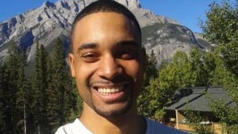 A man with a mountain background smiles at the camera. 