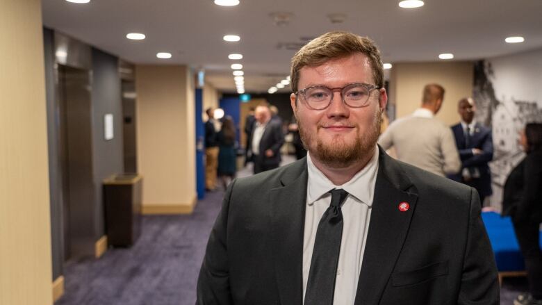 A man with a black tie and suit stands in a hallway