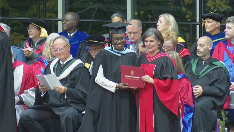 A smiling woman in a graduation cap and gown posing with a faculty member on a stage.