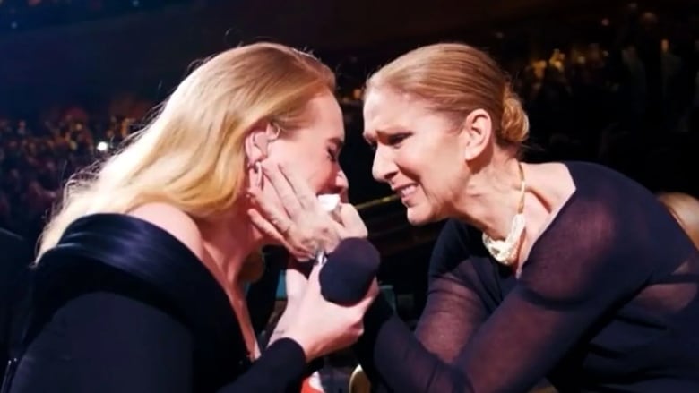 An emotional Adele and Celine, both wearing black dresses, hug each other during a concert. 