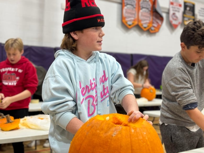 A boy in a hat puts his hand in a pumpkin