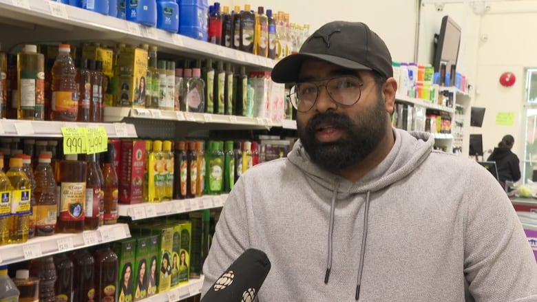 A South Asian man speaks in a supermarket aisle.