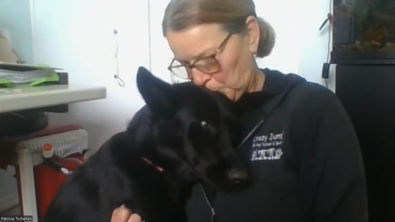 A woman kisses a black dog on its head