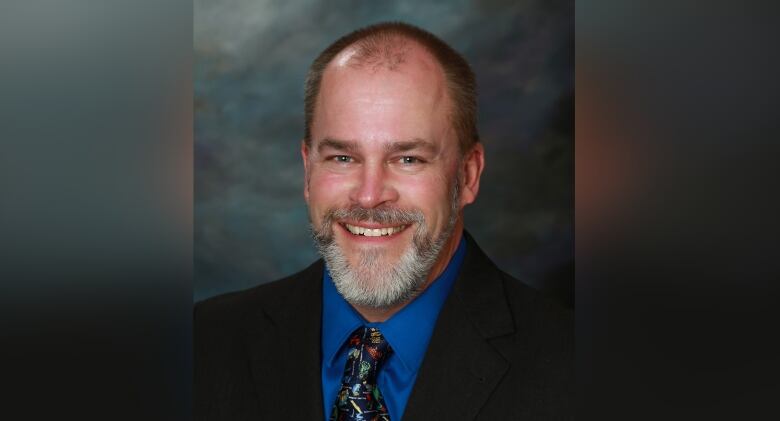 Bearded man in a dark suit smiling at the camera. 