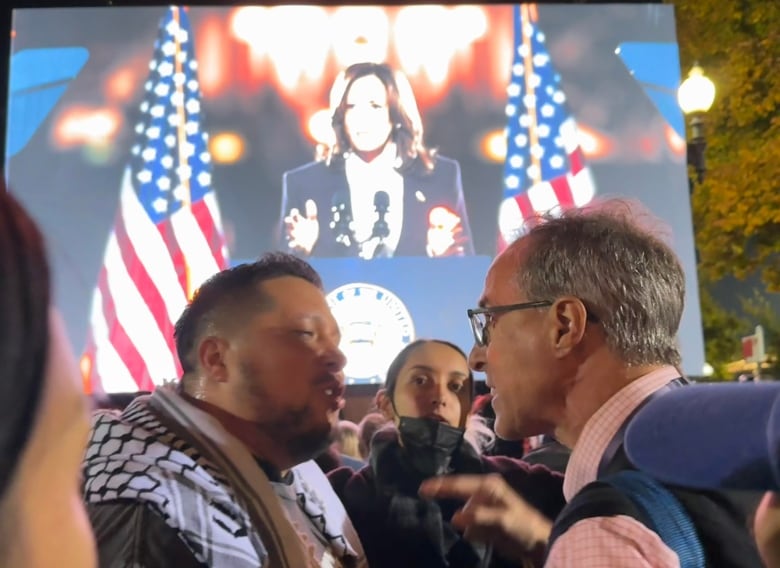 Two men face each other, appearing to be in conflict, both speaking and one is pointing. In the background, a video feed of Kamala Harris is projected.