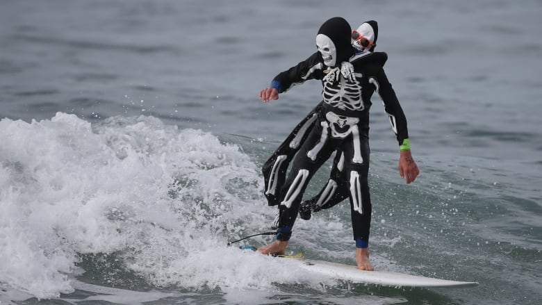 A surfer dressed as a skeleton rides a wave.