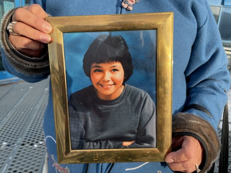 A framed photograph of a young girl, held by her sister 