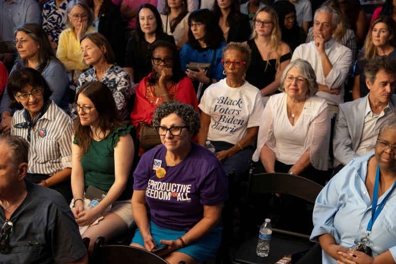 Women sit in rows in an audience listening to a politician speak.