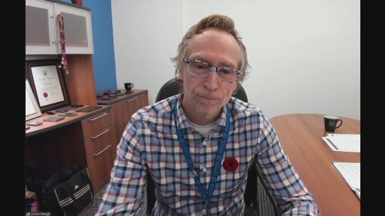 A man in a plaid shirt sits at his desk looking into a camera during a Zoom interview. 