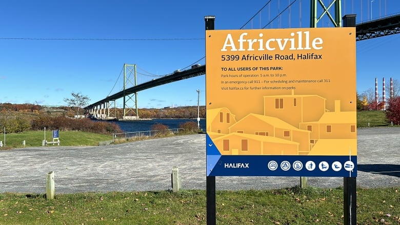 A yellow park sign with the word 'Africville' is shown in the foreground with the harbour behind and Halifax's MacKay bridge.