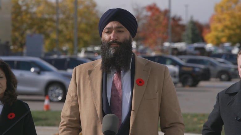 Photo of a man in a beige suit speaking outside to media