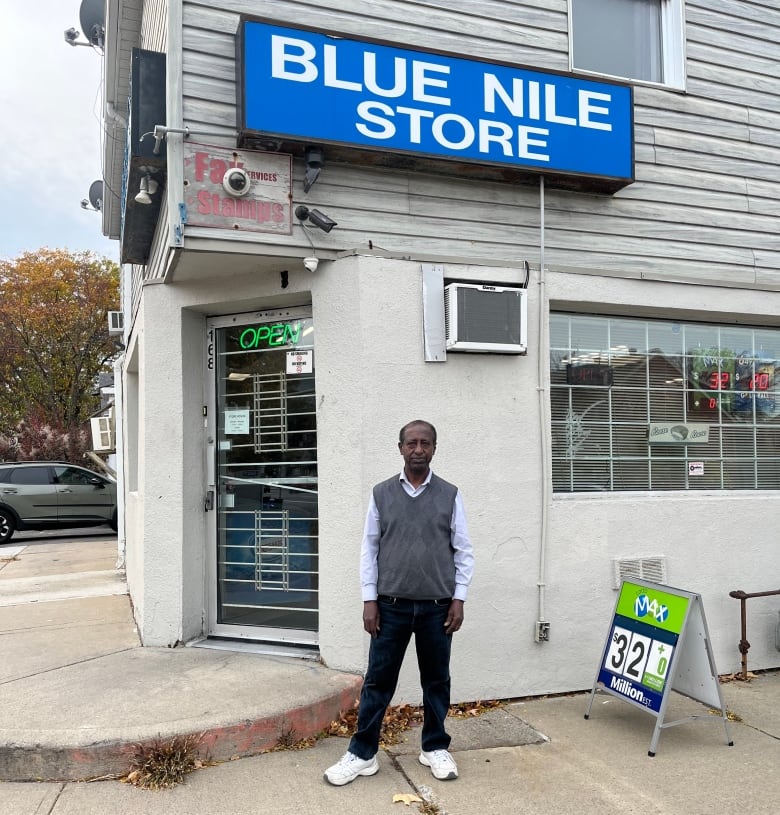 A man stands in front of a corner store.