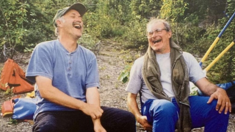 Two men sitting outside on lawn chairs, laughing.