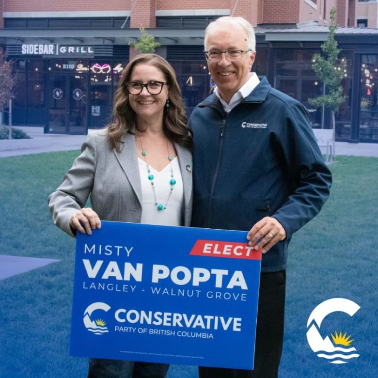 A woman with glasses and brown hair stands with a man with grey hair and glasses. They hold a  B.C. Conservative Party sign that reads Misty Van Popta.