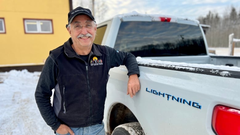 A man leans on a truck box smiling at the camera.