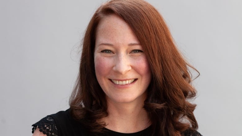 A woman with long auburn hair smiling at the camera and wearing a black top