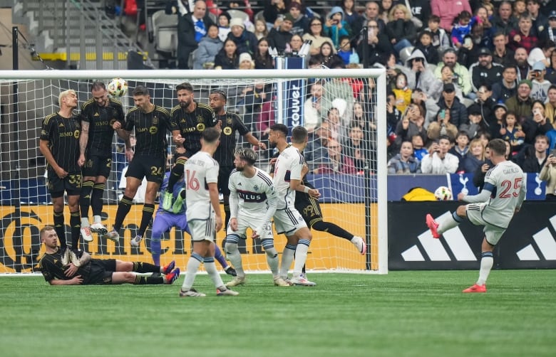 A soccer player takes a free kick as players stand like a wall in front of the goal post. 