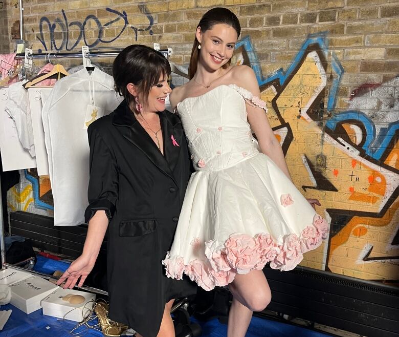 A woman with dark hair posing with a woman in a white and pink dress.