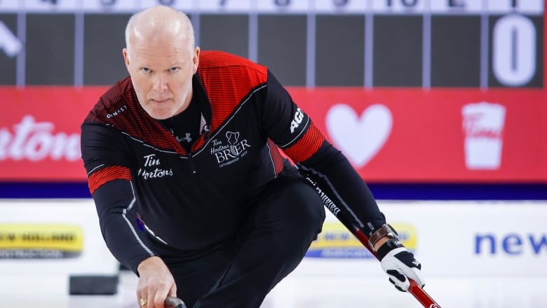 A man kneels on the ice while making a curling shot. 