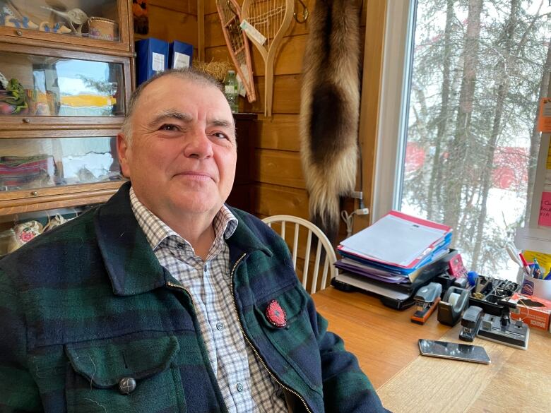 A man wearing a checkered shirt and a flannel jacket gives a slight smile at the camera. 