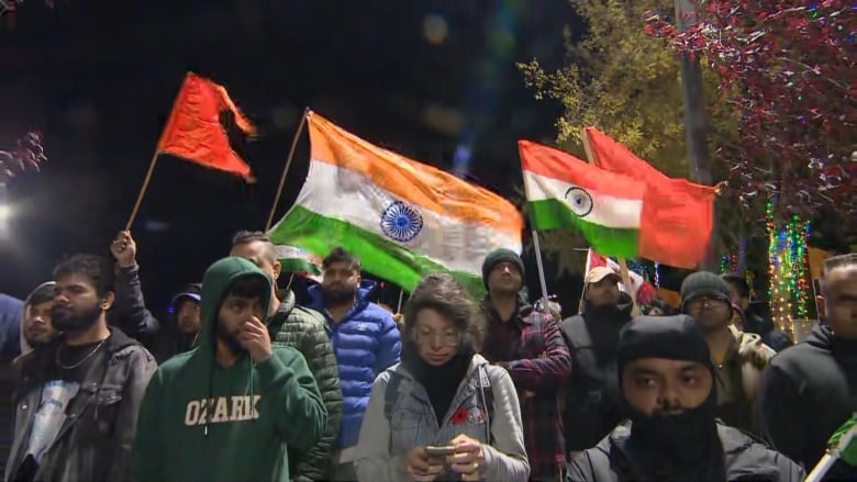 People wave Indian flags and religious flags at an outdoor rally.