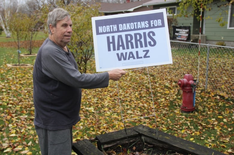 A man in a black and grey sweater holds a light blue sign that reads 