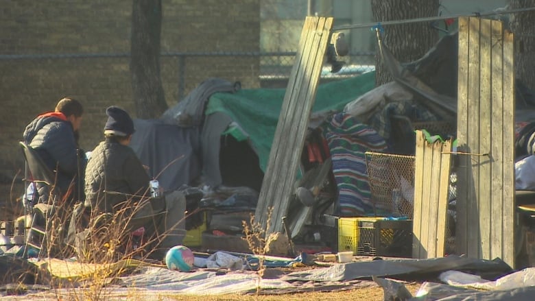 A few people are pictured at a homeless encampment.