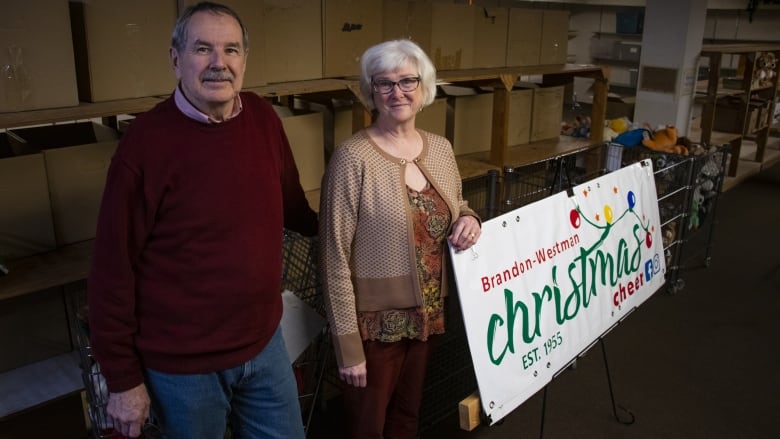 A man and woman stand beside a sign that says Brandon-Westman Christmas Cheer.