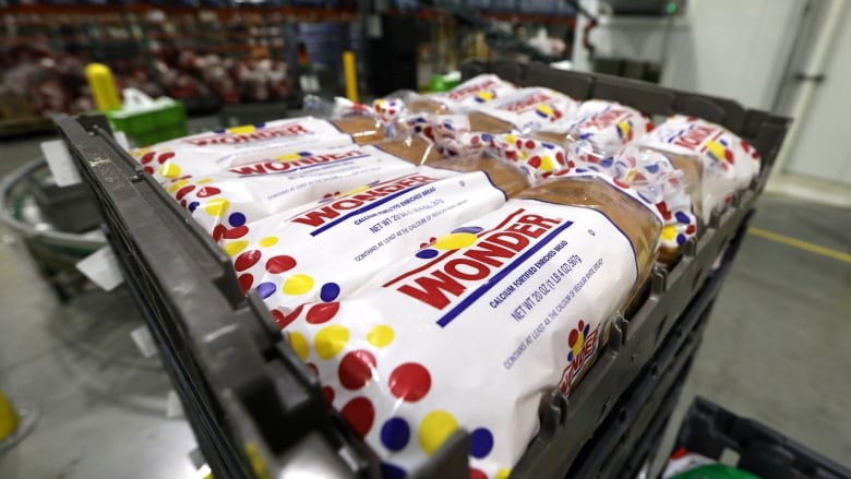 Several loaves of Wonder Bread are seen on a metal pallet in some sort of industrial-looking setting. The focus is on the corner of the bread label nearest to us, and everything beyond the pallet is blurry. 