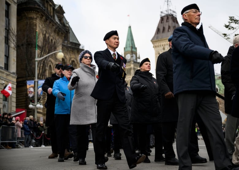 Middle-age military veterans march during a memorial ceremony on an autumn day.