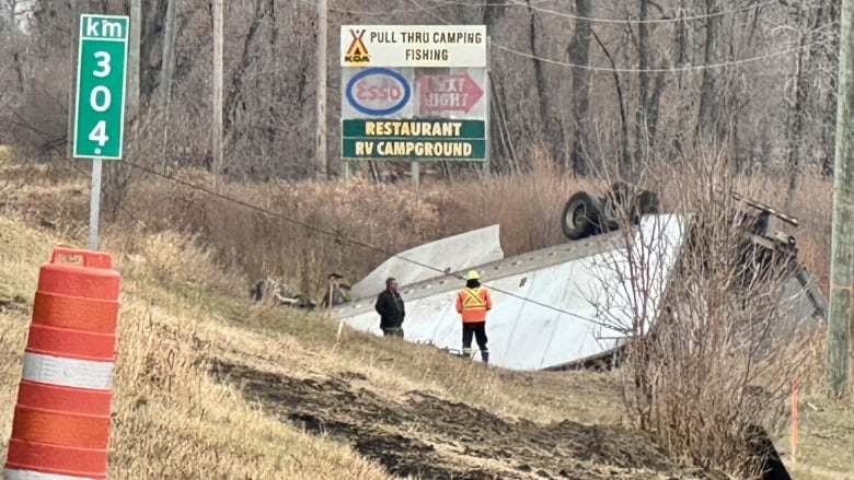 Semi-truck flipped upside down in the ditch by a highway.