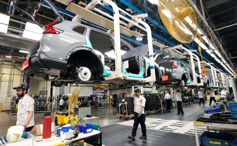 Workers in an automotive plant walk along a car assembly line.