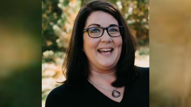 A woman with a black top and glasses smiles.