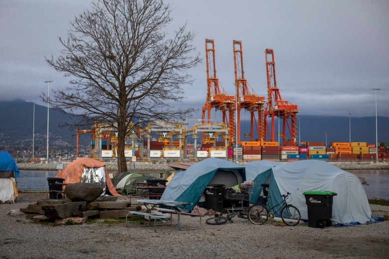 A cargo port with loaders and shipping terminals looms over a series of small tents and tarps.