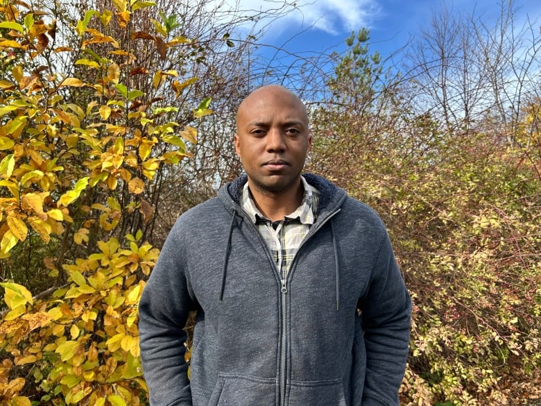 A man stands in front of some greenery .