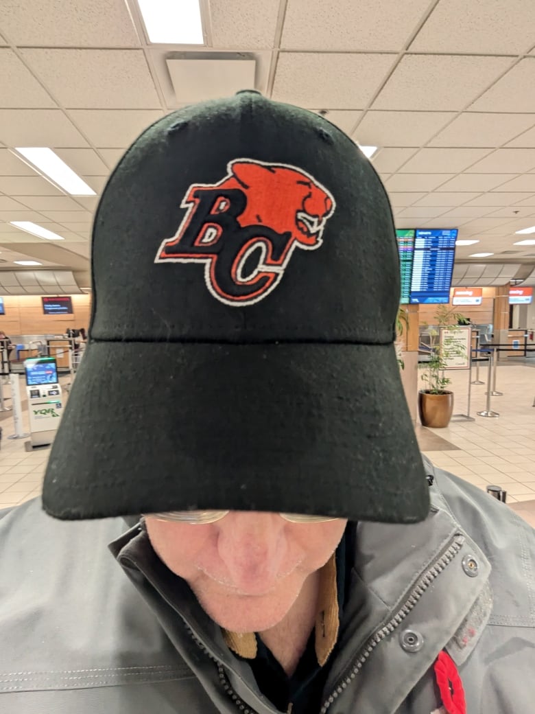 A man shows off his black cap reading B.C. with the symbol of a lion roaring. 