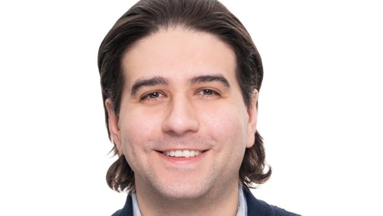 A headshot of a man with dark hair who is smiling 