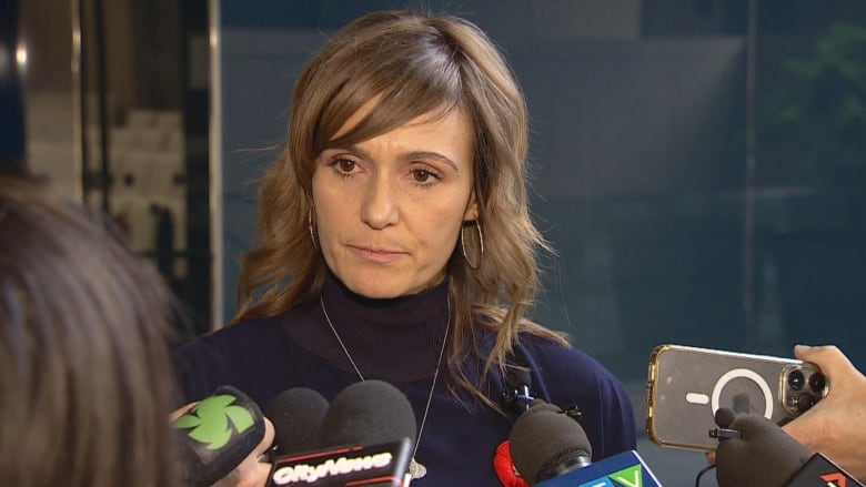 A woman stands in front of a collection of microphones.