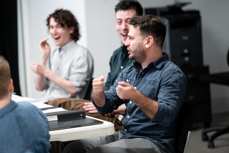 Three men laugh while sitting around a table.