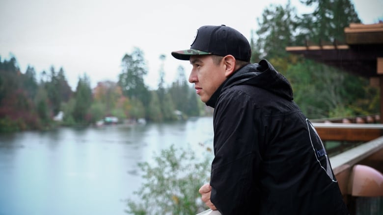 A man leans on a railing, looking out over the water.