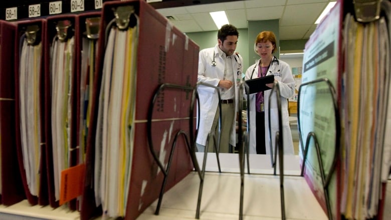 A physician is seen between patient records as she uses an iPad while speaking with a resident.