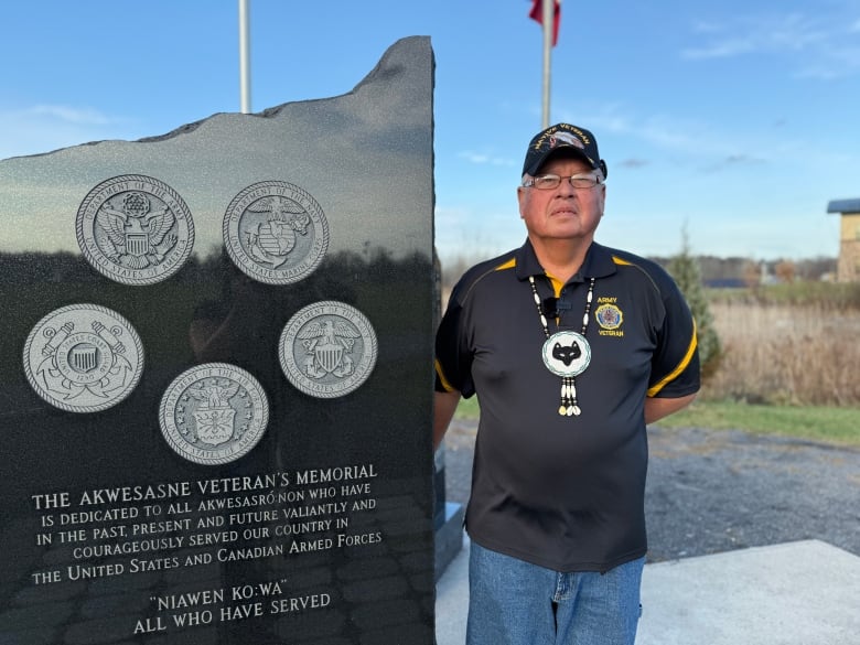 Vet stands beside monument w clans. 