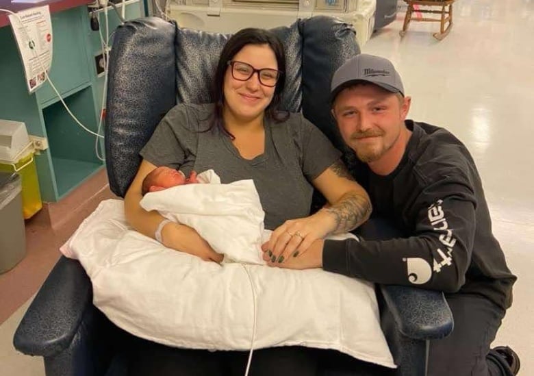 A couple poses for a photo with their newborn baby in a hospital.