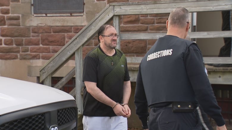 A man in shackles is led from a courthouse to a police vehicle. 