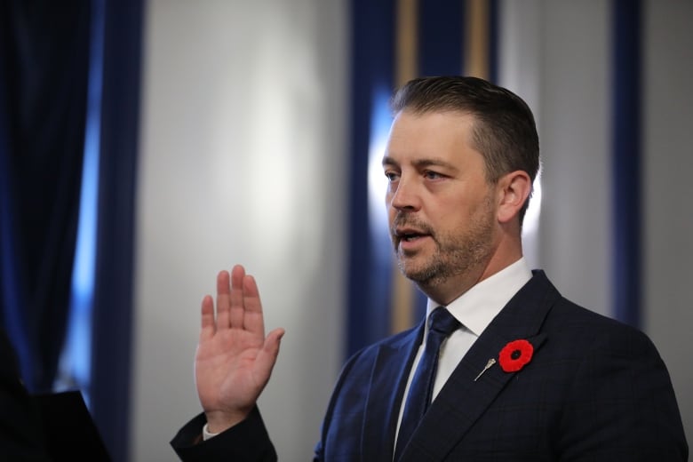 A man in a blue suit raises his right hand. 