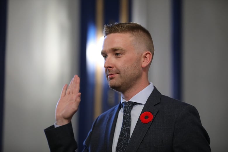 A man in a dark suit raises his right hand.