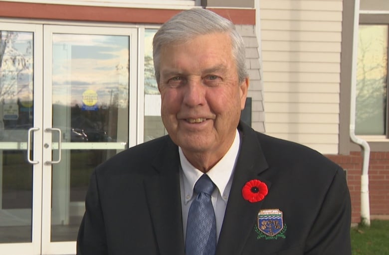 man in dark suit, white shirt and tie, gray hair, smiles to camera. 