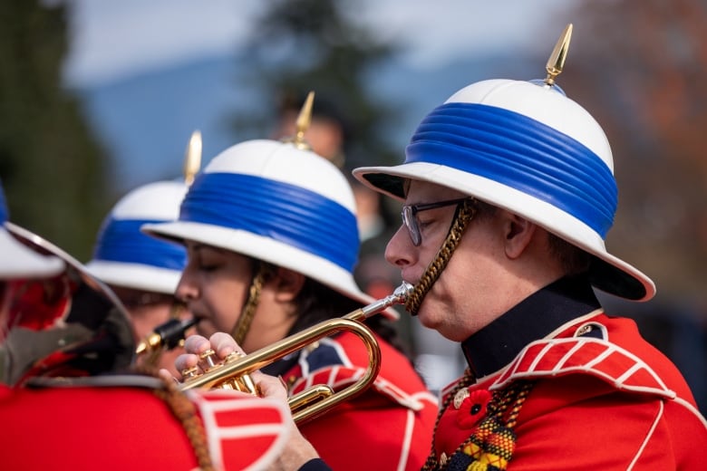 People wearing red military uniforms play trumpets.