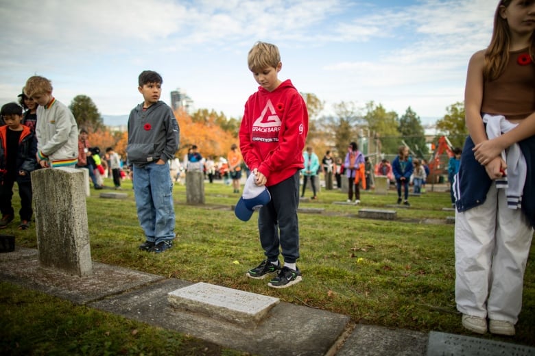 Children stand and bow their heads near headstones.